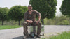 A hunter sits on a ZARGES K424 XC aluminum case with wheels and talks through why he uses it, then rolls it across gravel